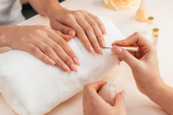 Bottle of Kodi Natural Beige Rubber Base Gel with a brush and manicured nails in the background.